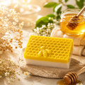 Jabón artesanal de miel con Vitamina E sobre una piedra con miel en un tarro y flores decorativas.